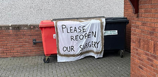 Handwritten sign that says Please Reopen Our Surgery hung over some bins